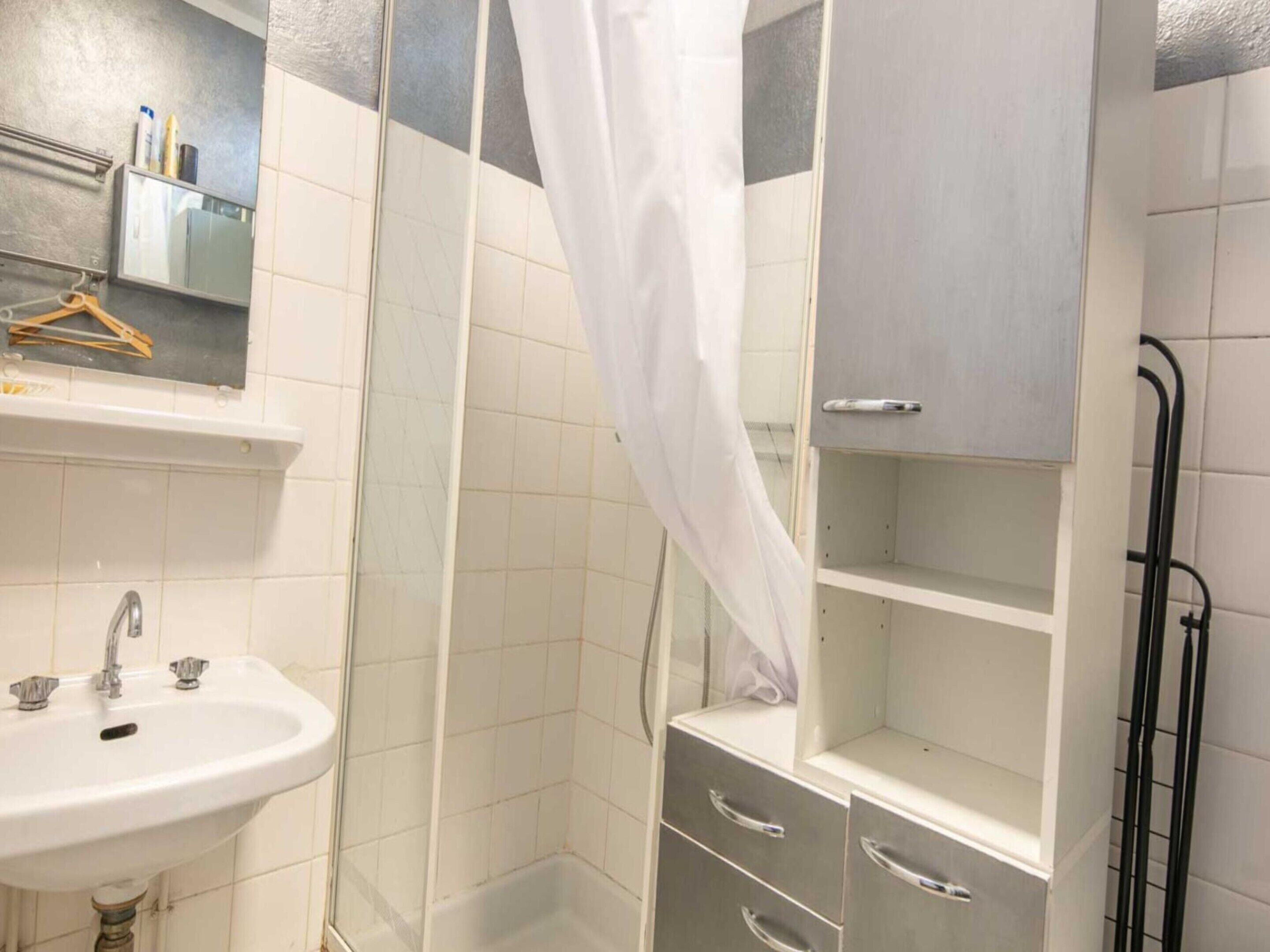A bathroom with a sink, a shower with a curtain, and a cabinet with drawers.