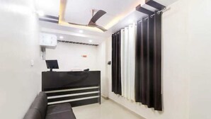 Un área de recepción con un mostrador negro, un sofá negro, un ventilador de techo y cortinas negras.