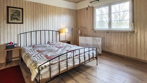 A bedroom with a wooden ceiling, a bed with a metal frame, a bedside table with a lamp, a window with curtains, and a framed picture on the wall. - Mit großem Garten by Interhome (Hohenbucko)