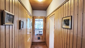 A hallway with wooden paneling, framed pictures on the walls, a patterned rug, and a window at the end. - Mit großem Garten by Interhome (Hohenbucko)