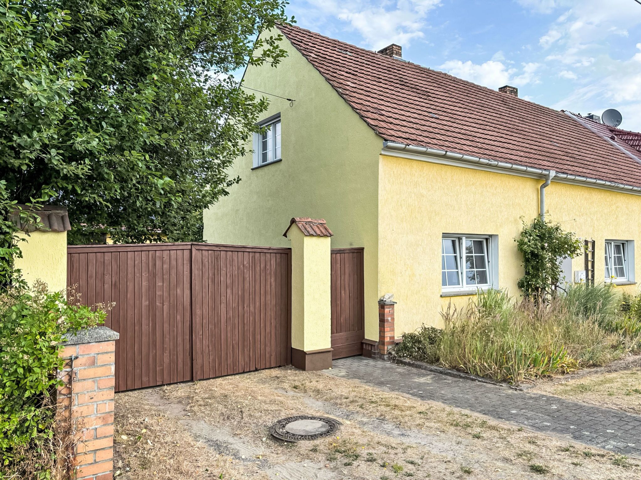 A two-story house with a brown gate, a brick pillar, and a paved driveway.