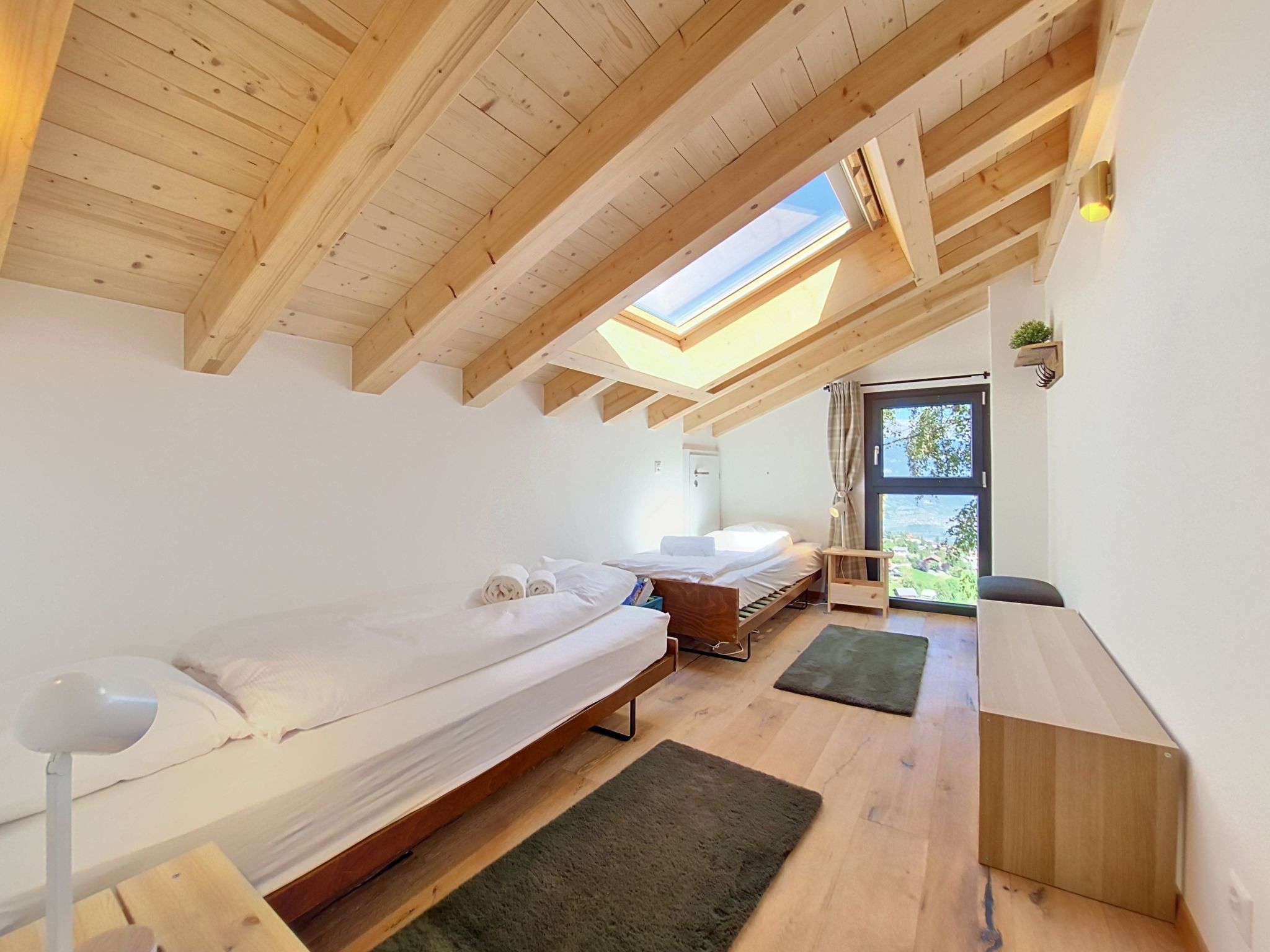 Una camera da letto con due letti, una scrivania e un lucernario.