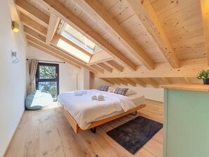 A bedroom with a skylight, wooden beams, a bed with pillows, a bedside table, and a view of the outdoors. - Byzance by Interhome (Nendaz)