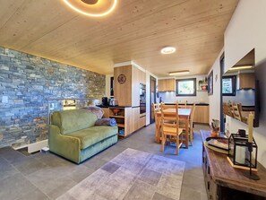 A compact living space with a stone wall, a sofa, a dining table with chairs, and a kitchen area. - Byzance by Interhome (Nendaz)