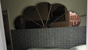 Un dormitorio con cama, mesita de noche de madera, espejo y suelo de baldosas.