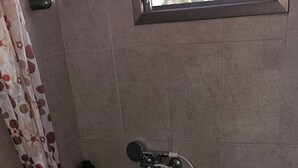 Un baño con inodoro, bañera con ducha y lavamanos, además de un ventanal sobre la bañera.