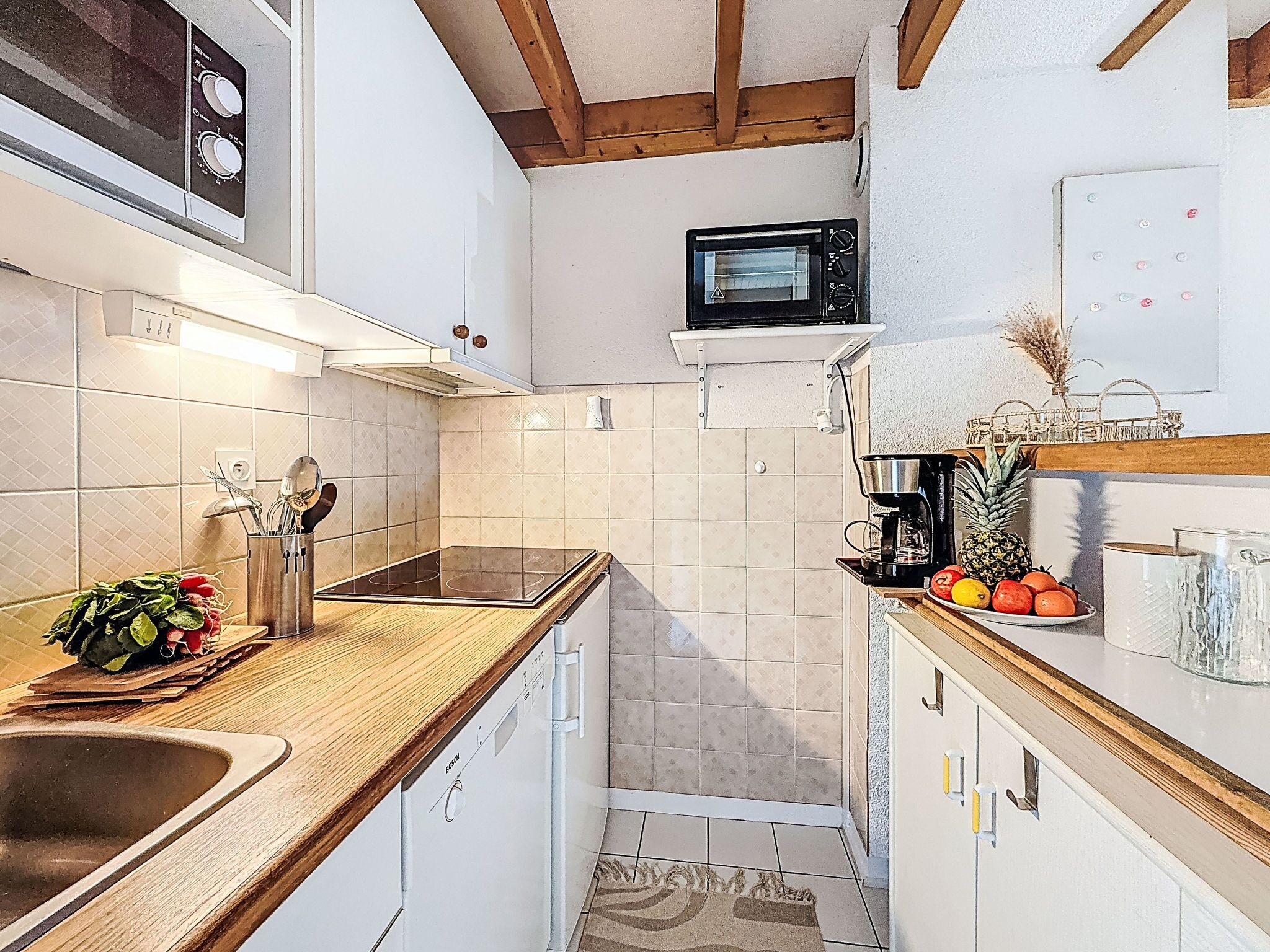 A compact kitchen with a built-in microwave, a coffee maker, and a fruit bowl.