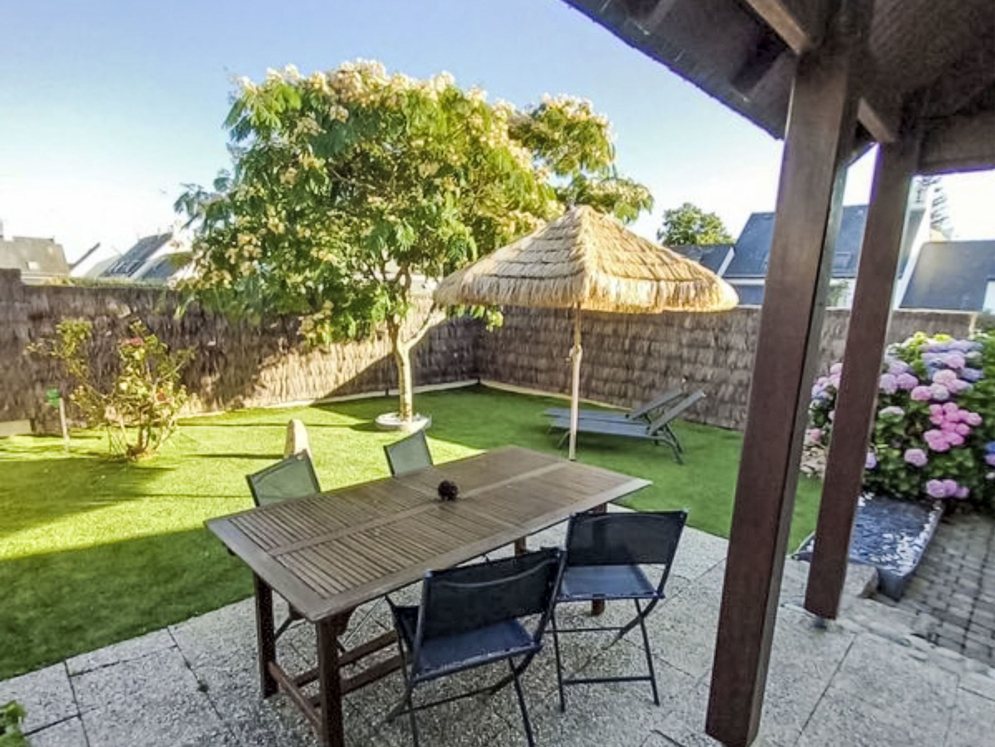 Eine Terrasse mit Tisch und Stühlen, einem Reetdachschirm, einem Baum und einer Backsteinmauer.