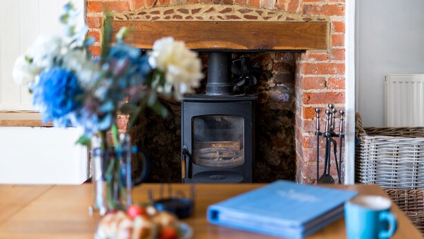 Un ambiente acogedor con una chimenea de ladrillo, una mesa con un plato de comida, un jarrón de flores y un libro azul.