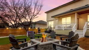 Ein Garten mit Feuerstelle, Sitzgelegenheiten im Freien und einer Holzterrasse.
