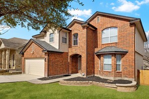 A two-story brick house with a garage, a front porch, and a landscaped yard. - Game Night Central! Game Room, Fire Pit, Pool Access Near BMT & SeaWorld (San Antonio)