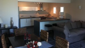 Eine moderne Küche mit weißen Schränken, einer zentralen Kochinsel und einem Essbereich mit Korbstühlen und einem Tisch.