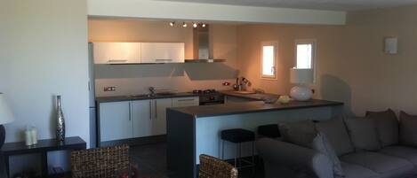 A modern kitchen with white cabinets, a central island, and a dining area with wicker chairs and a table.