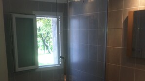 Ein modernes Badezimmer mit einer Duschkabine aus Glas, einem Fenster mit Blick ins Grüne und einem Holzwaschtisch mit Waschbecken.