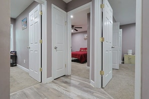 A hallway with white doors, a ceiling fan, and a bed with a red blanket in the background.