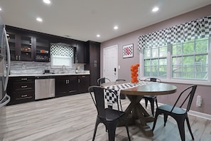 A modern kitchen with dark cabinetry, a dishwasher, and a dining area with a checkered tablecloth.