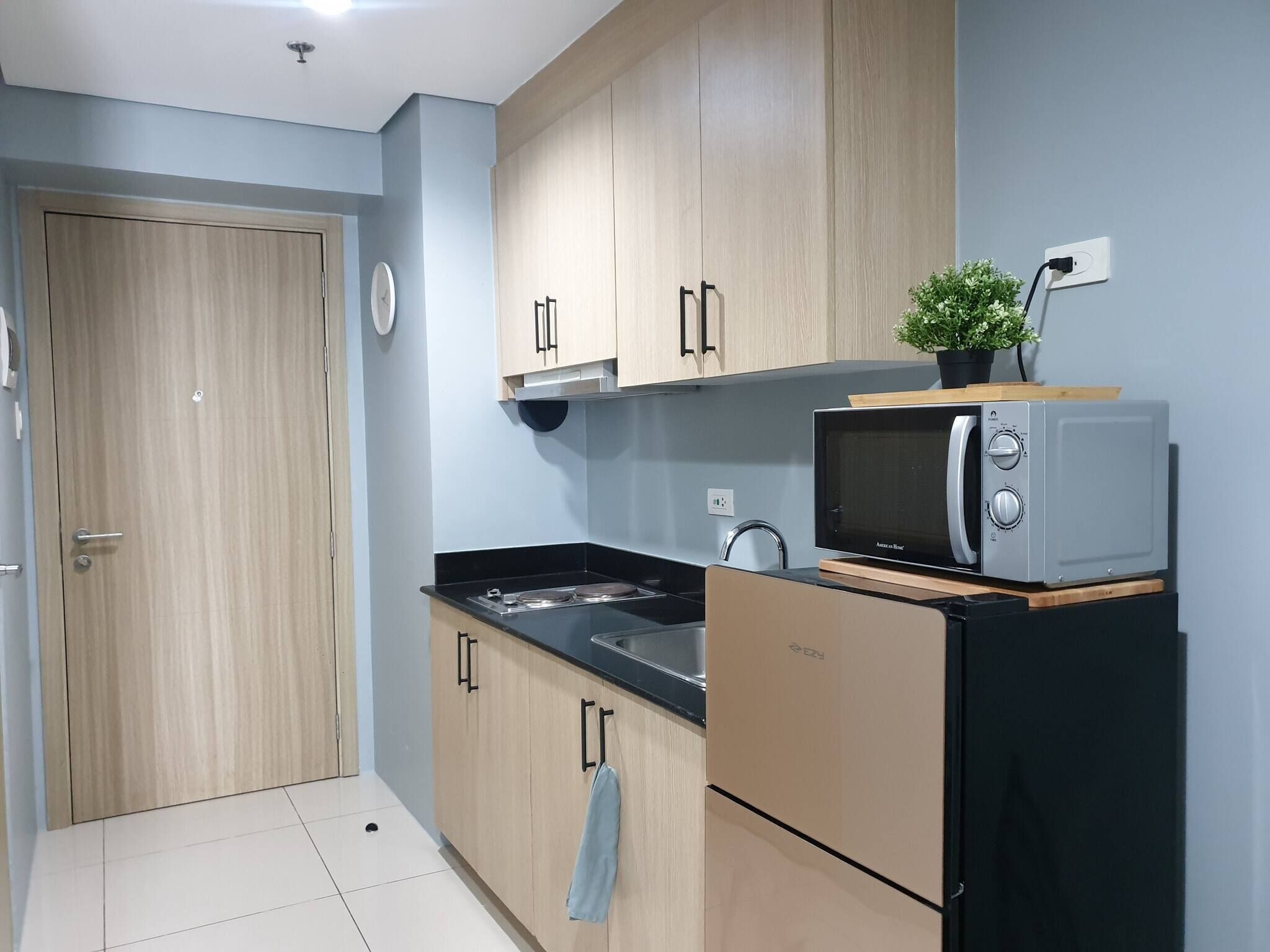 A compact kitchen with wooden cabinets, a black countertop, a microwave, and a small potted plant.