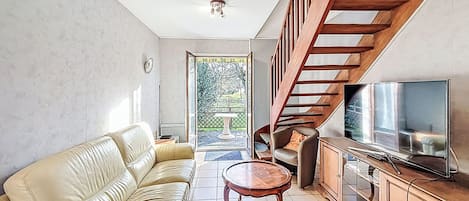 Ein Wohnzimmer mit einer Couch, einem Fernseher, einer Holztreppe und Blick ins Freie.