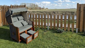 Un fauteuil de jardin en osier, doté d’un auvent, placé sur une pelouse verdoyante, avec une clôture en bois et une rivière en arrière-plan.