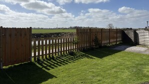Une clôture en bois, une zone herbeuse et un ciel dégagé avec quelques nuages.