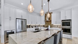 A modern kitchen with white cabinetry, stainless steel appliances, a marble island, and pendant lighting. - SunnySide: Private beach steps away, FREE Golf Cart, Heated pool, Luxury home (Destin)