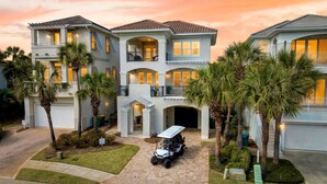 A multi-story residential building with a driveway, palm trees, and a golf cart. - SunnySide: Private beach steps away, FREE Golf Cart, Heated pool, Luxury home (Destin)