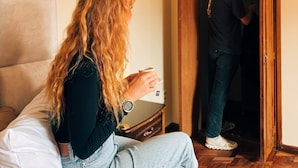 Une pièce avec un lit, une armoire en bois et une personne debout dans l’encadrement de la porte.