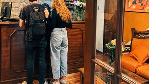 Un espace d’accueil avec un mur en pierre, un comptoir d’accueil en bois et un coin salon agrémenté d’un canapé orange.