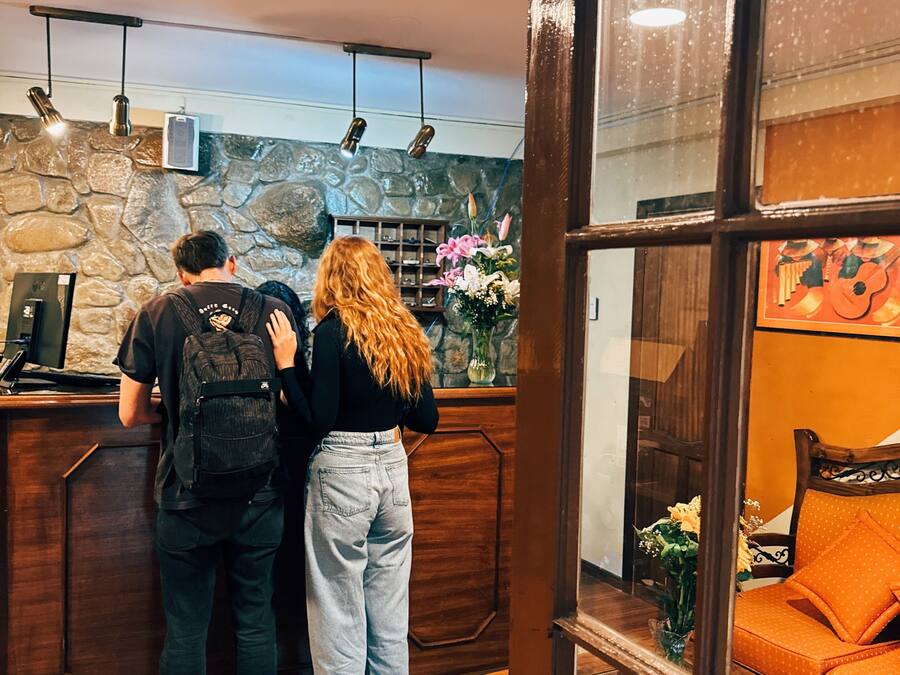 Un área de recepción con pared de piedra, mostrador de madera y zona de estar con un sofá naranja.