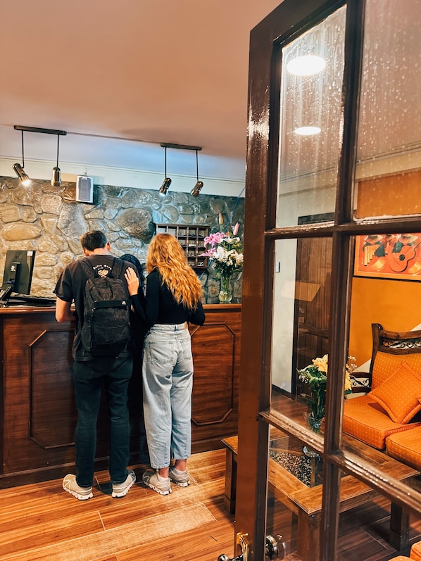 Un espace d’accueil avec un mur en pierre, un comptoir d’accueil en bois et un coin salon agrémenté d’un canapé orange.