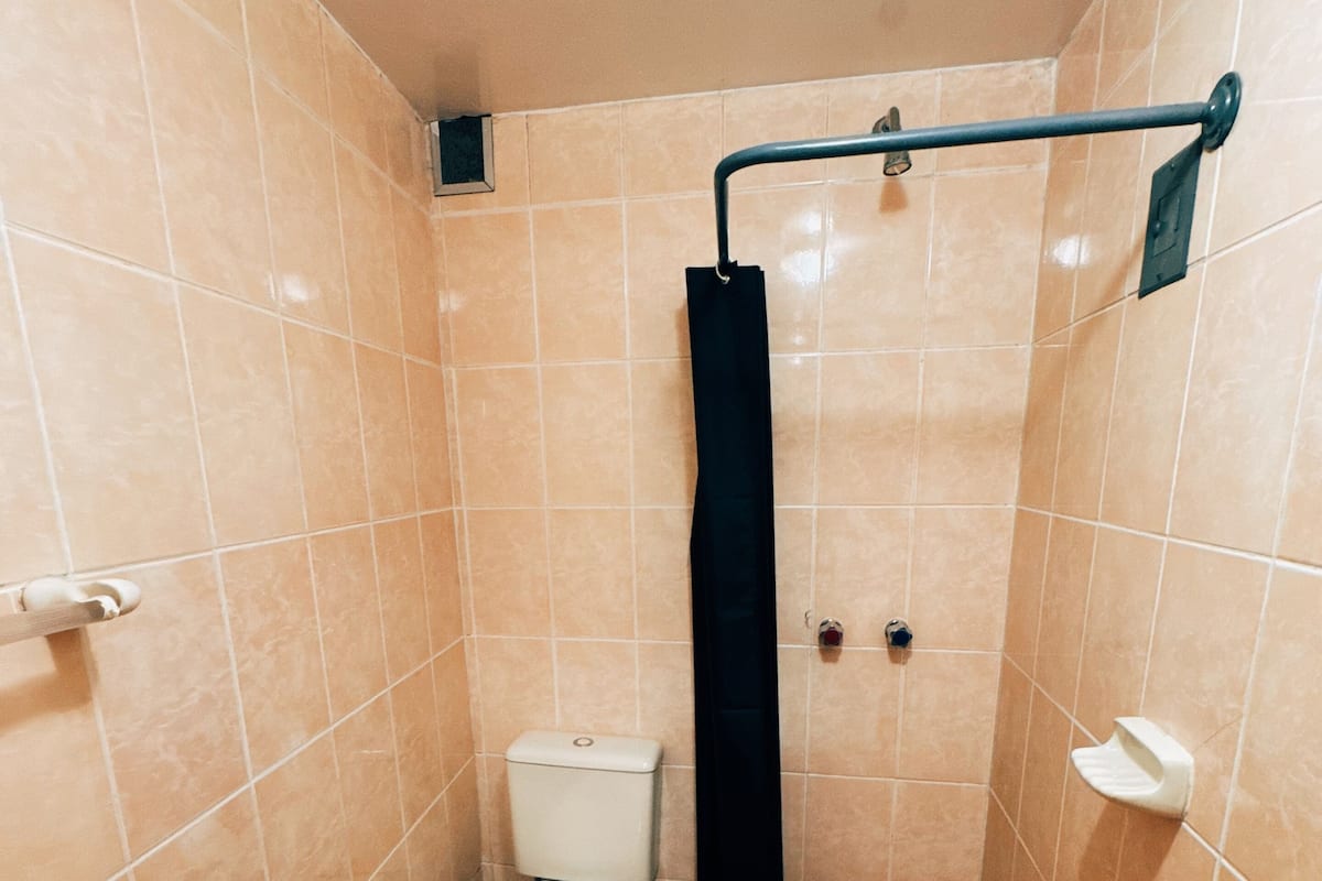 A small, tiled bathroom with a toilet, a shower curtain, a trash bin, and a towel dispenser.