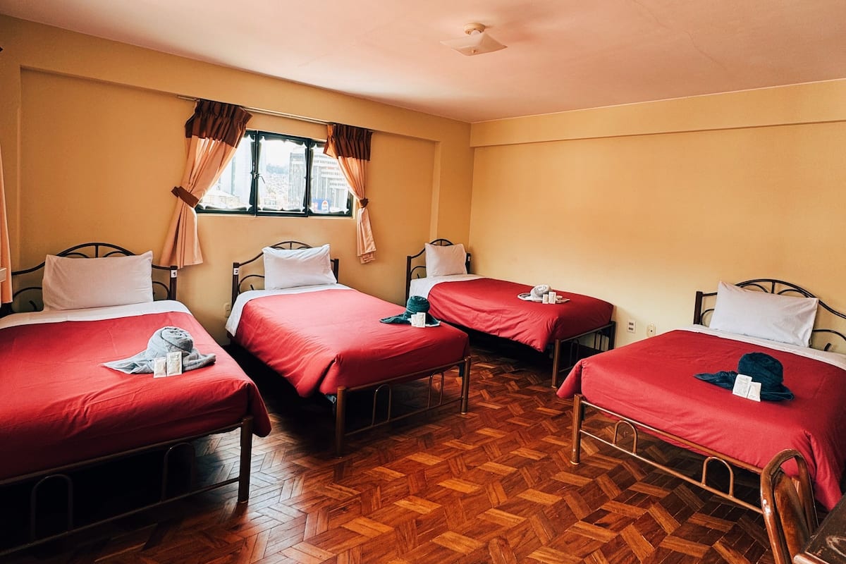 A room with four beds, each with red bedding, wooden flooring, and a window with curtains.
