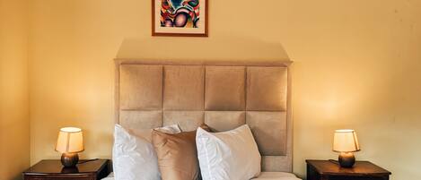 A hotel room with a large bed, two bedside tables, a headboard, and a framed artwork on the wall.