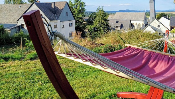 A hammock in a grassy area with a view of houses and a church in the background. - SOUTH1 - Peace and quiet between Moselle and Hunsrück (Grenderich)