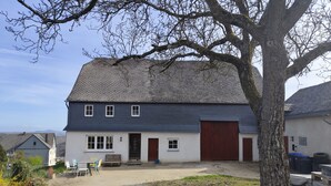A two-story house with a large garage, a gravel driveway, and a tree in the foreground. - SOUTH1 - Peace and quiet between Moselle and Hunsrück (Grenderich)