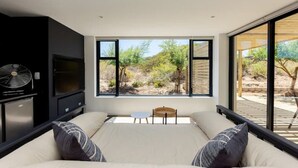 A bedroom with a large bed, a small table, and a view of a desert landscape through large windows.