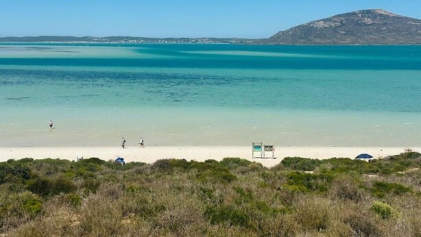 A beach with clear turquoise water, a sandy shore, and a mountain in the background.
