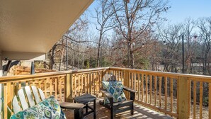 Eine Holzterrasse mit zwei Adirondack-Stühlen und einem Tisch, mit Blick auf eine bewaldete Gegend.