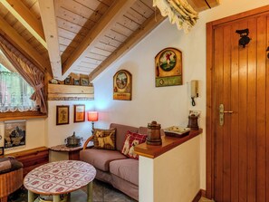 A cozy room with a wooden ceiling, a wooden door, a sofa, a table, and various wall decorations including framed pictures and a clock. - Apartment Fresia by Interhome (Spiazzo)