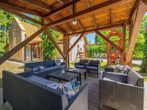 An outdoor patio with wicker furniture, a wooden pergola, and a stone building in the background. - Petka 1 by Interhome (Badacsonyörs)