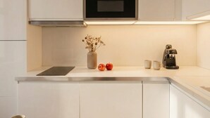 Ett modernt kök med vita skåp, en inbyggd ugn, en kaffebryggare och en vas med torkade blommor.