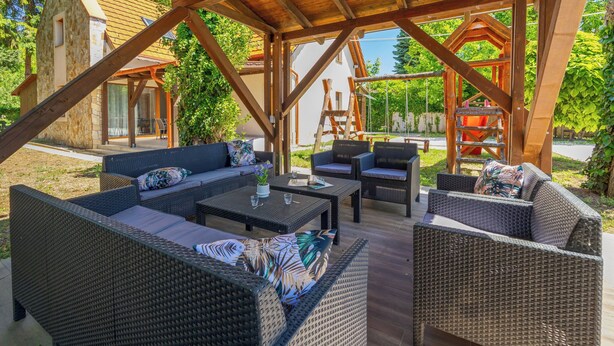 An outdoor patio with wicker furniture, a wooden pergola, and a stone building in the background. - Petka 2 by Interhome (Badacsonyörs)