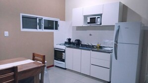 Una cocina compacta con alacenas blancas, un microondas, una estufa y un refrigerador.
