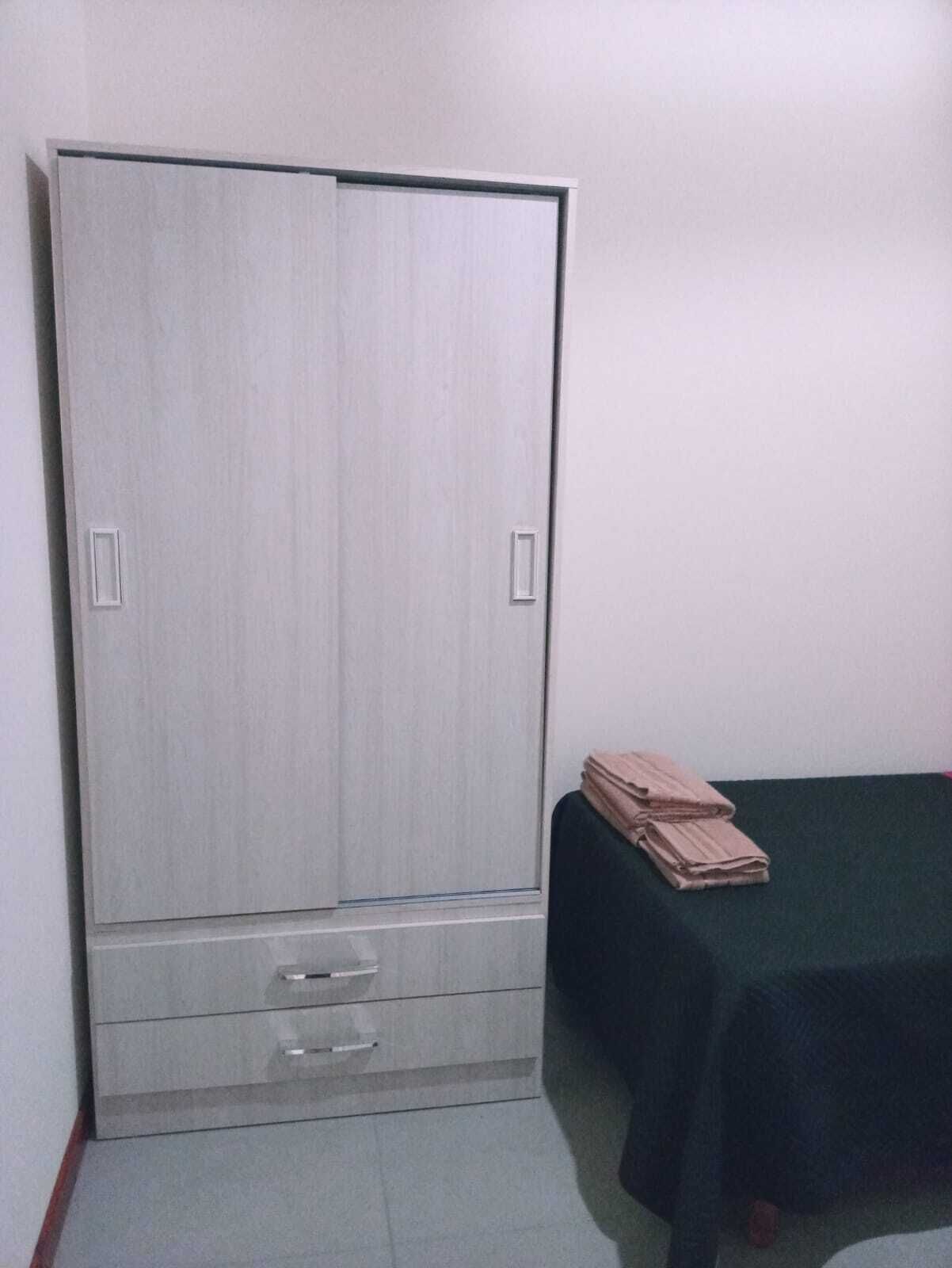Une chambre dotée d’une grande armoire, d’un lit recouvert d’une couvre-lit vert foncé et d’une petite table sur laquelle sont pliées des serviettes.