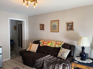 Un salon avec un canapé marron foncé, des coussins à motifs, une lampe de table en dentelle et des œuvres d’art encadrées accrochées au mur.