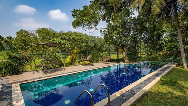 Una piscina rectangular con agua azul cristalina, rodeada por una solana empedrada y una cerca de metal.