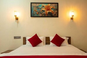 Une chambre d’hôtel avec un lit, deux oreillers rouges, un tableau au mur et deux lampes fixées au mur.