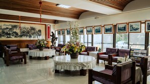 A hotel lobby with round tables, purple chairs, a large painting, and framed pictures on the wall. - tienhsiang youth activity center (Xiulin)