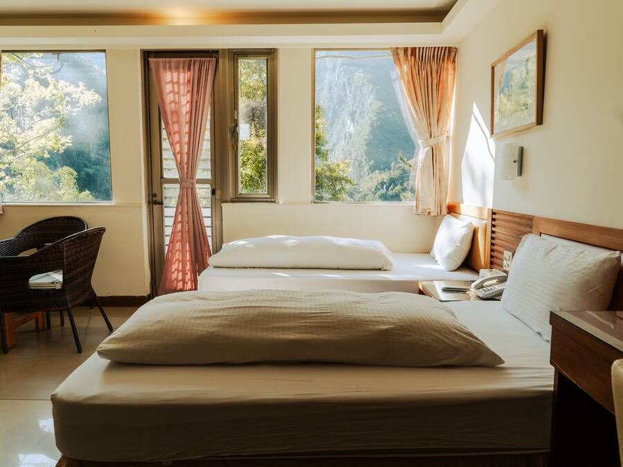 A hotel room with a bed, a chair, a desk, and large windows with curtains.