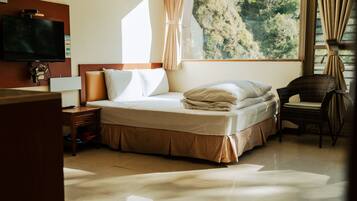 A hotel room with a bed, a television, a window with curtains, and a chair.